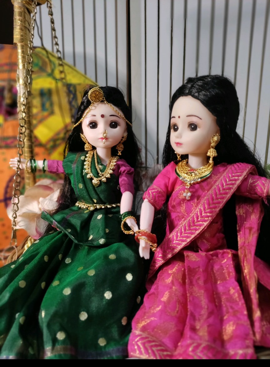 Two traditional Indian dolls in festive lehengas seated on a decorated swing